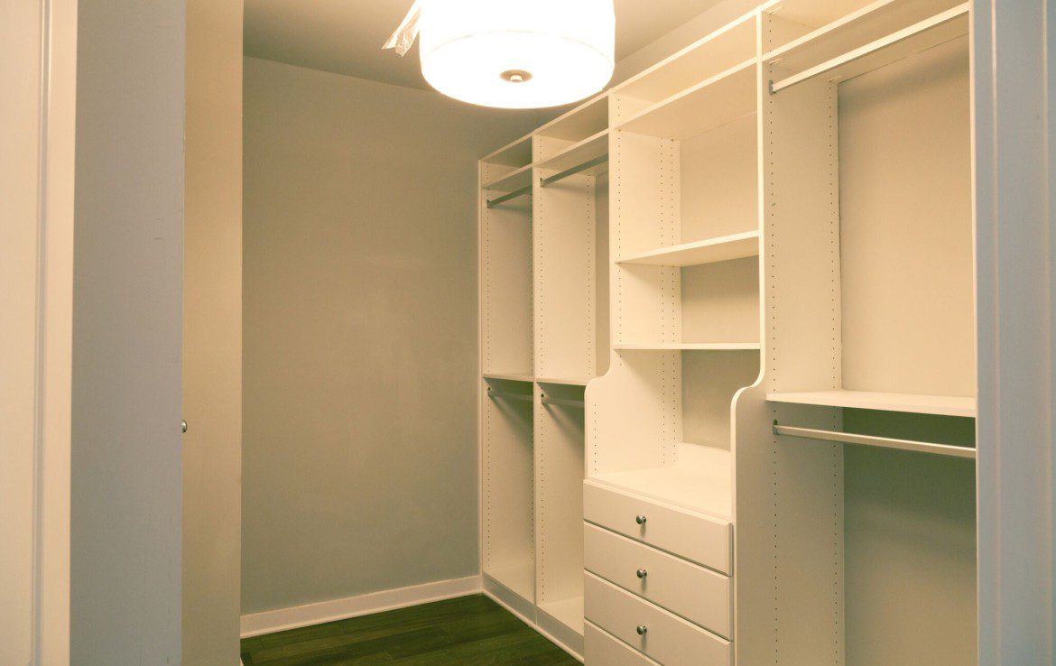 A walk in closet with white shelves and a light fixture.