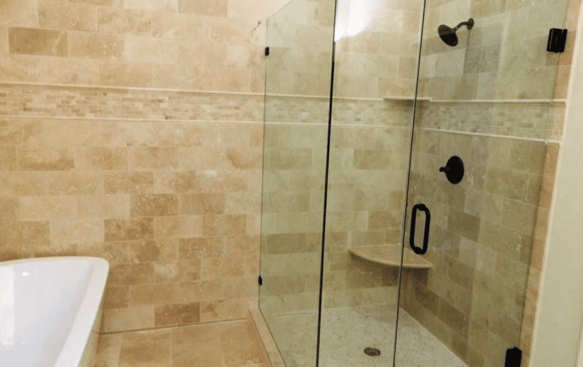 A beige tiled bathroom with a glass shower stall.