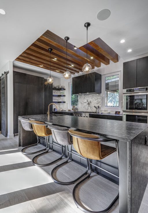A modern kitchen with black counter tops and wooden ceiling.