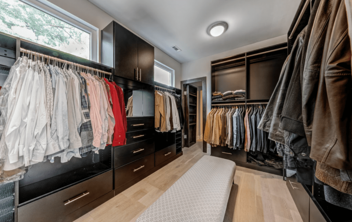 A walk - in closet with a bench and lots of clothes.