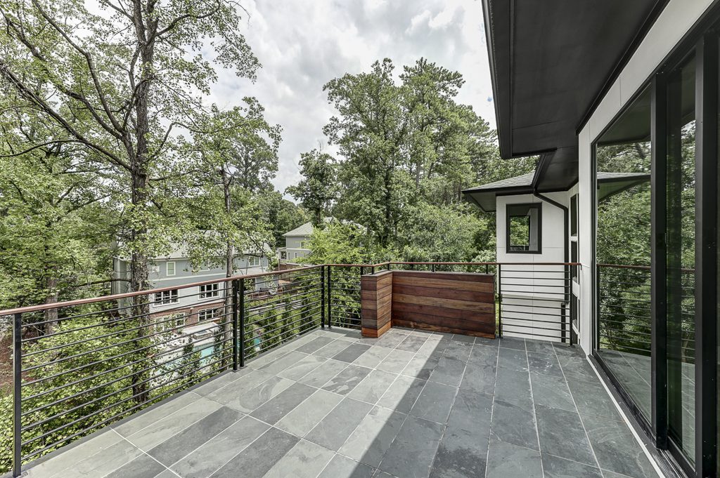 A balcony overlooking a wooded area with a glass railing.