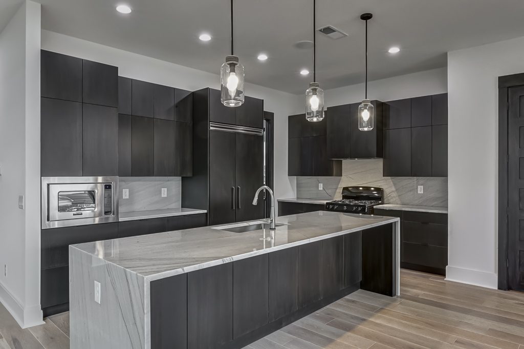 A kitchen with black cabinets and marble counter tops.